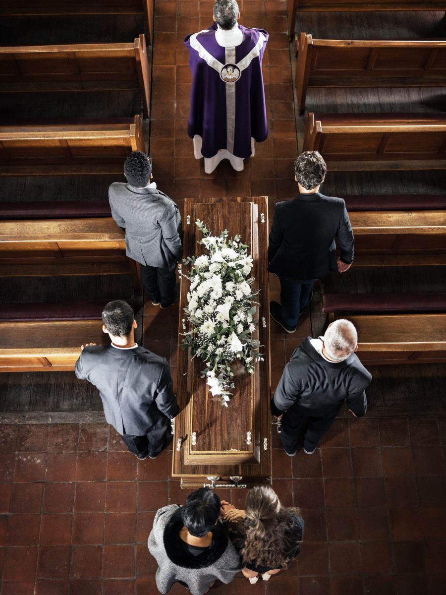 Funeral, church and sad people carrying coffin with a priest, pallbearers and church pew from above